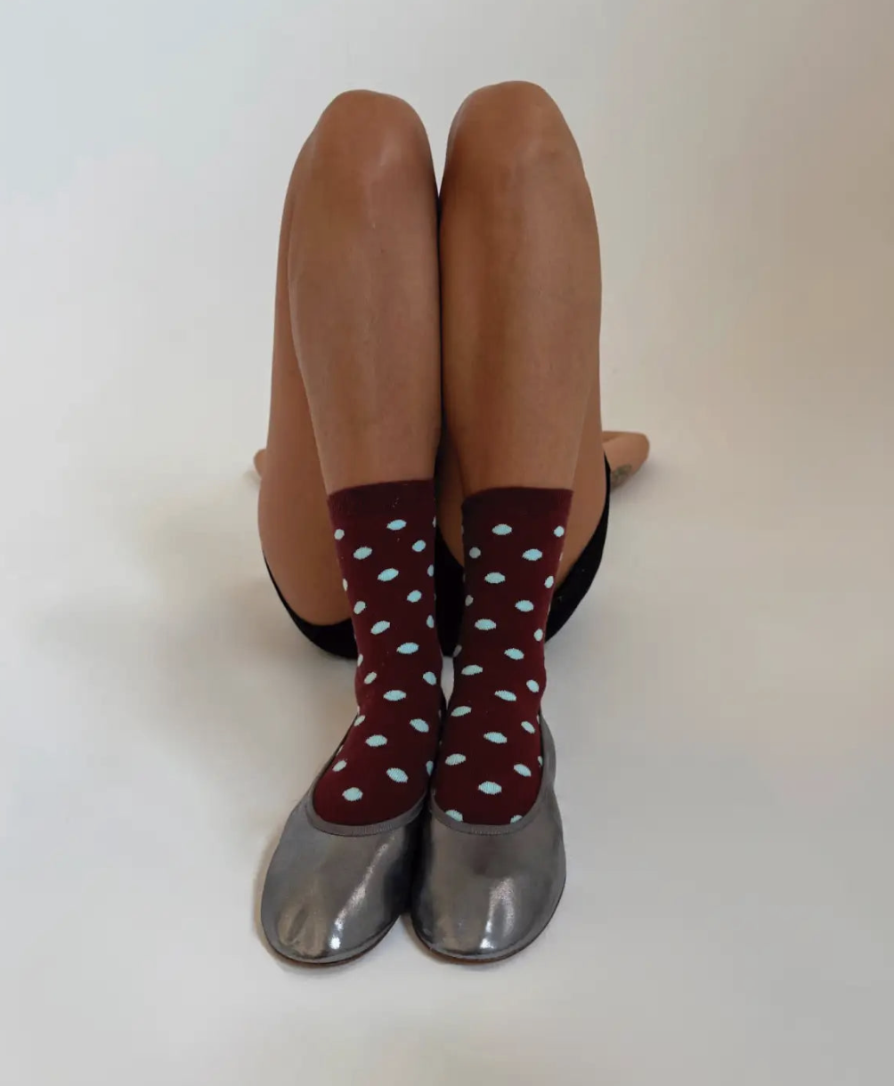 Maroon polka dot socks with light blue dots worn with silver metallic ballet flats, legs bent at knees