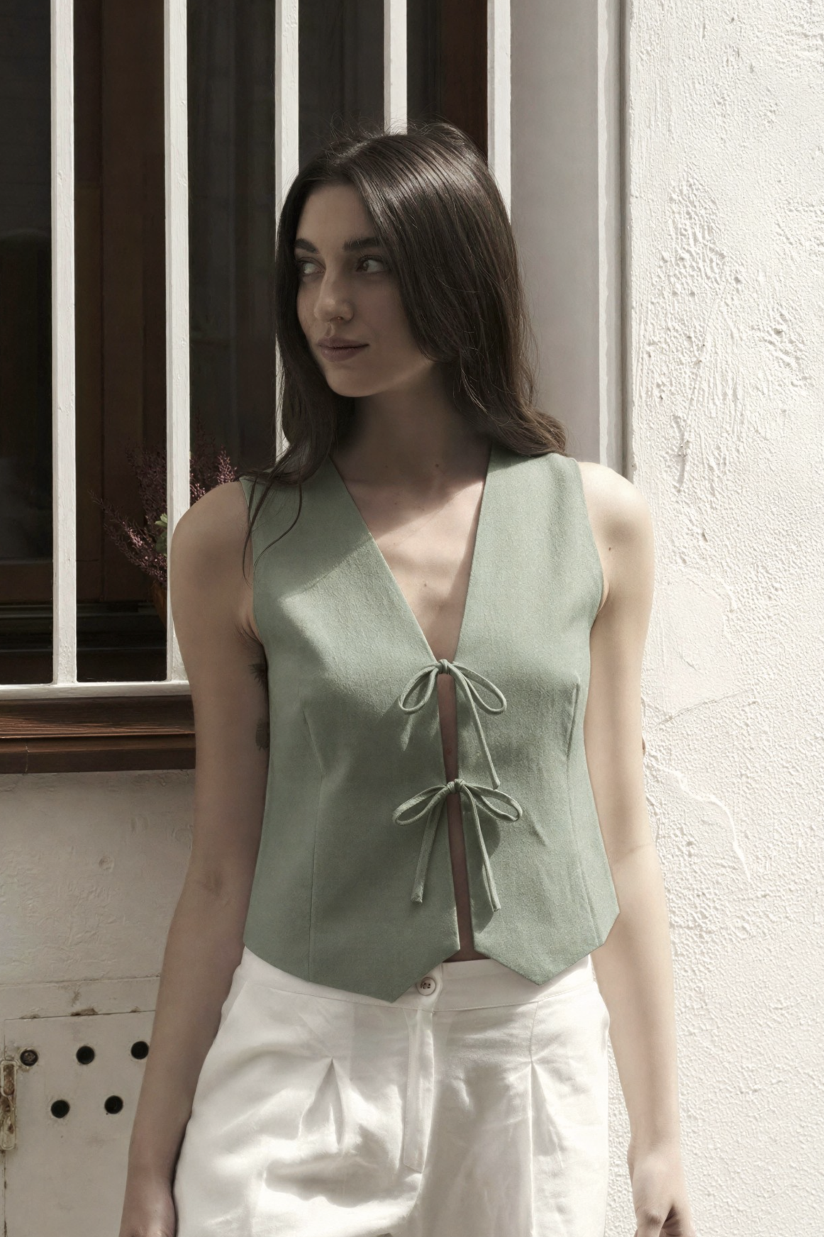 Sage green linen vest top with V-neck and tie front detail, paired with white trousers