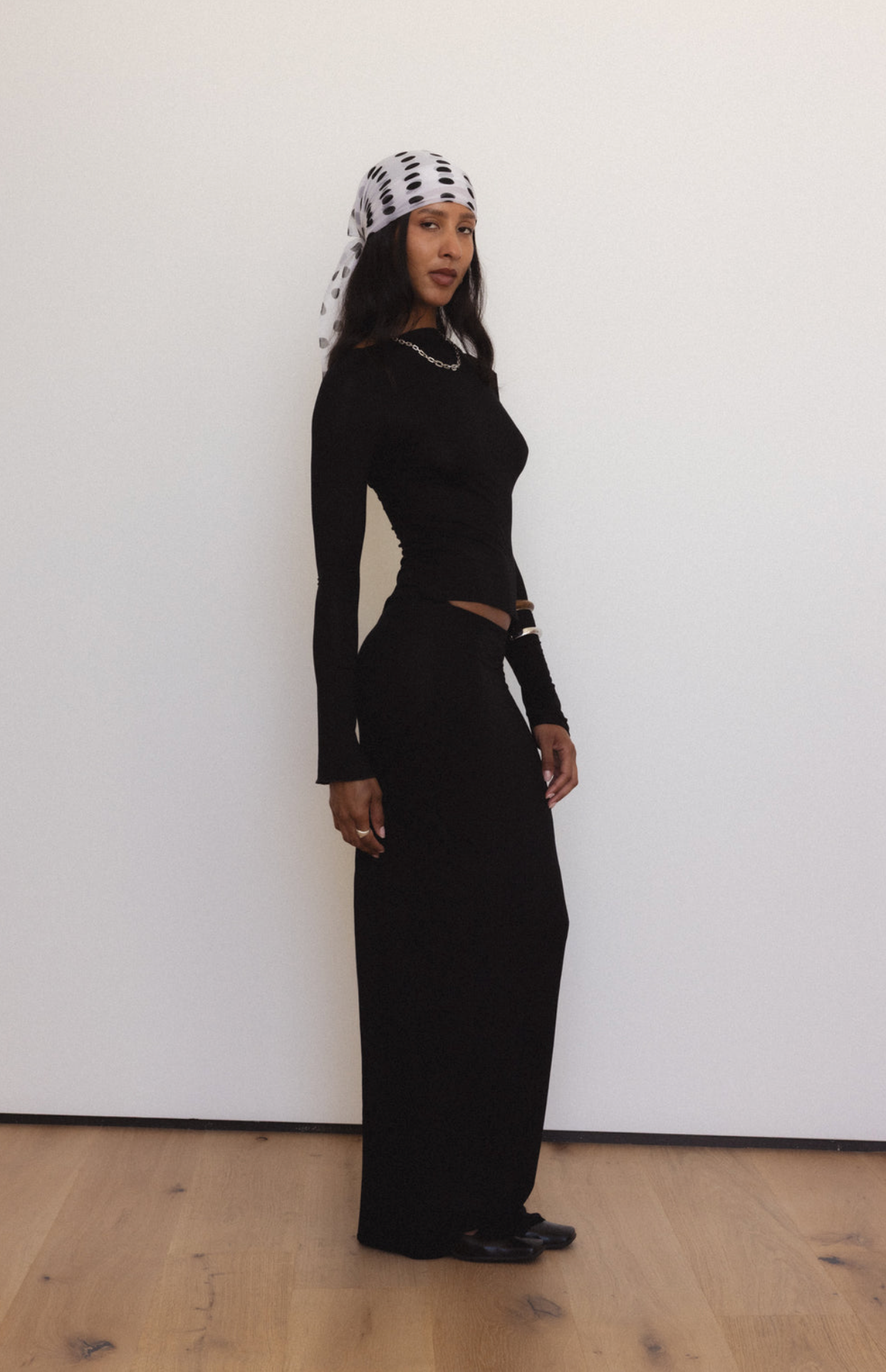 Woman wearing black long-sleeve cutout maxi dress with chain detail neckline and white patterned headscarf