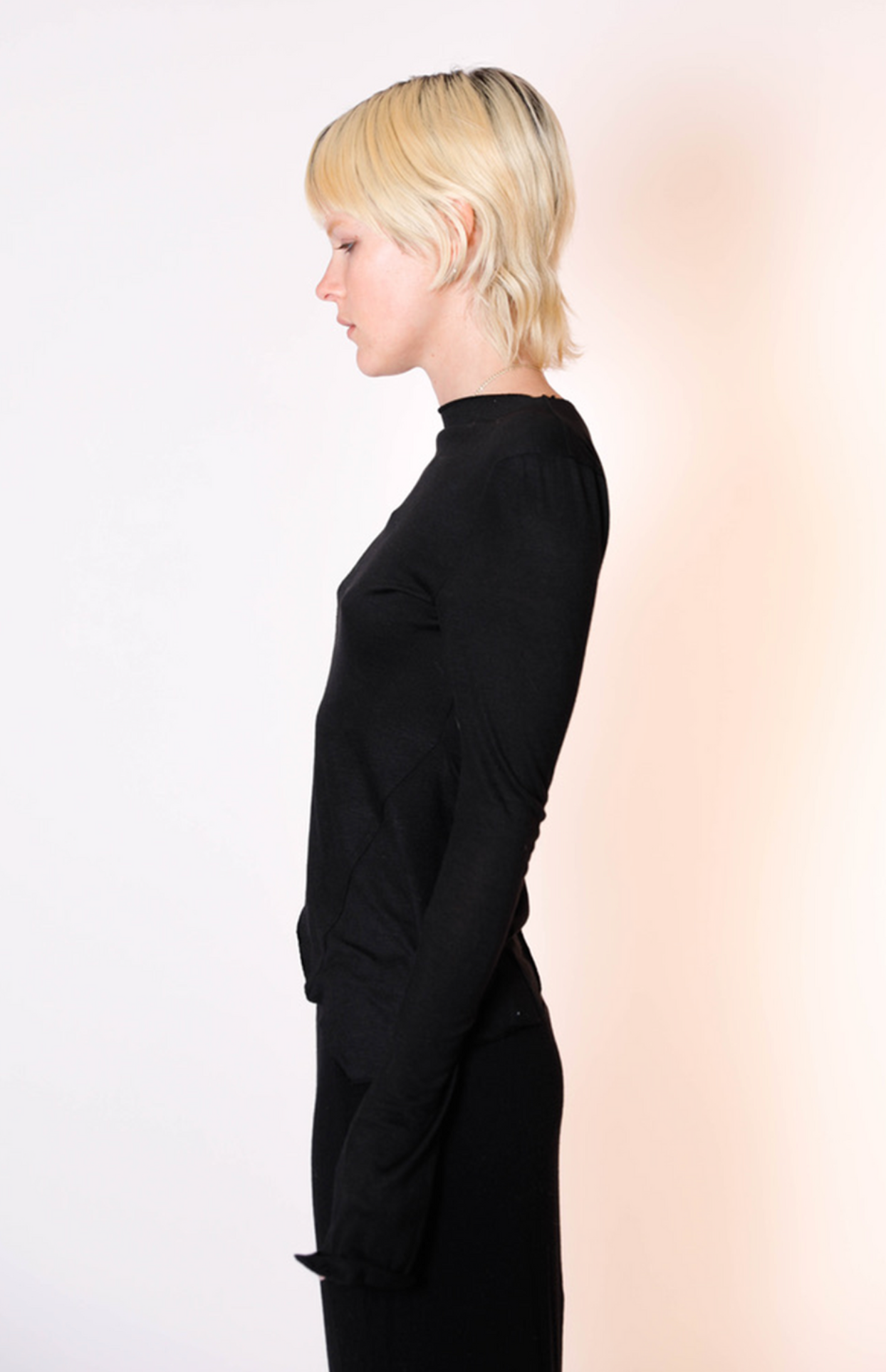 Black long-sleeve mock neck top in soft fabric, shown in profile view on model with blonde hair