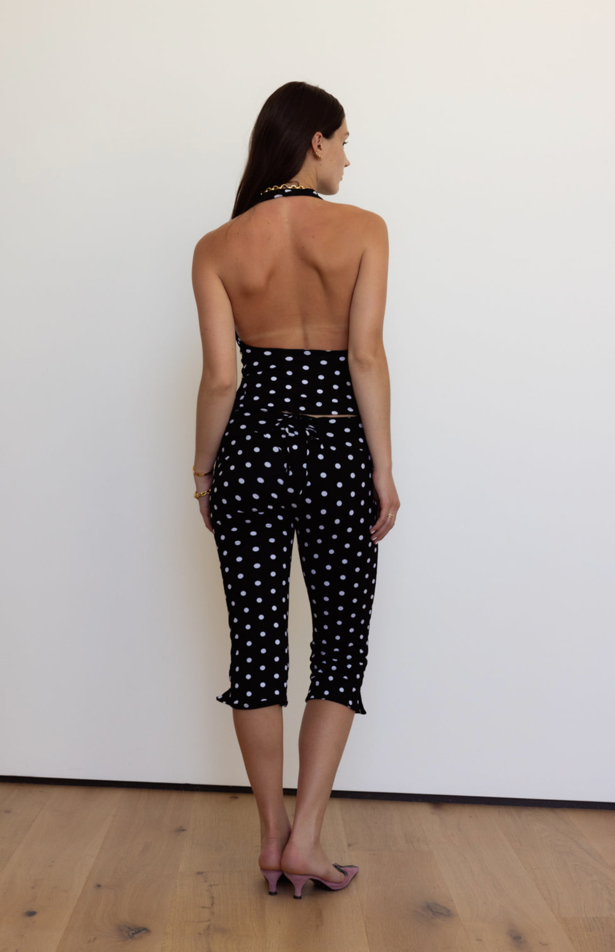 Black polka dot halter jumpsuit with open back and cropped ruffle hem legs, worn from behind