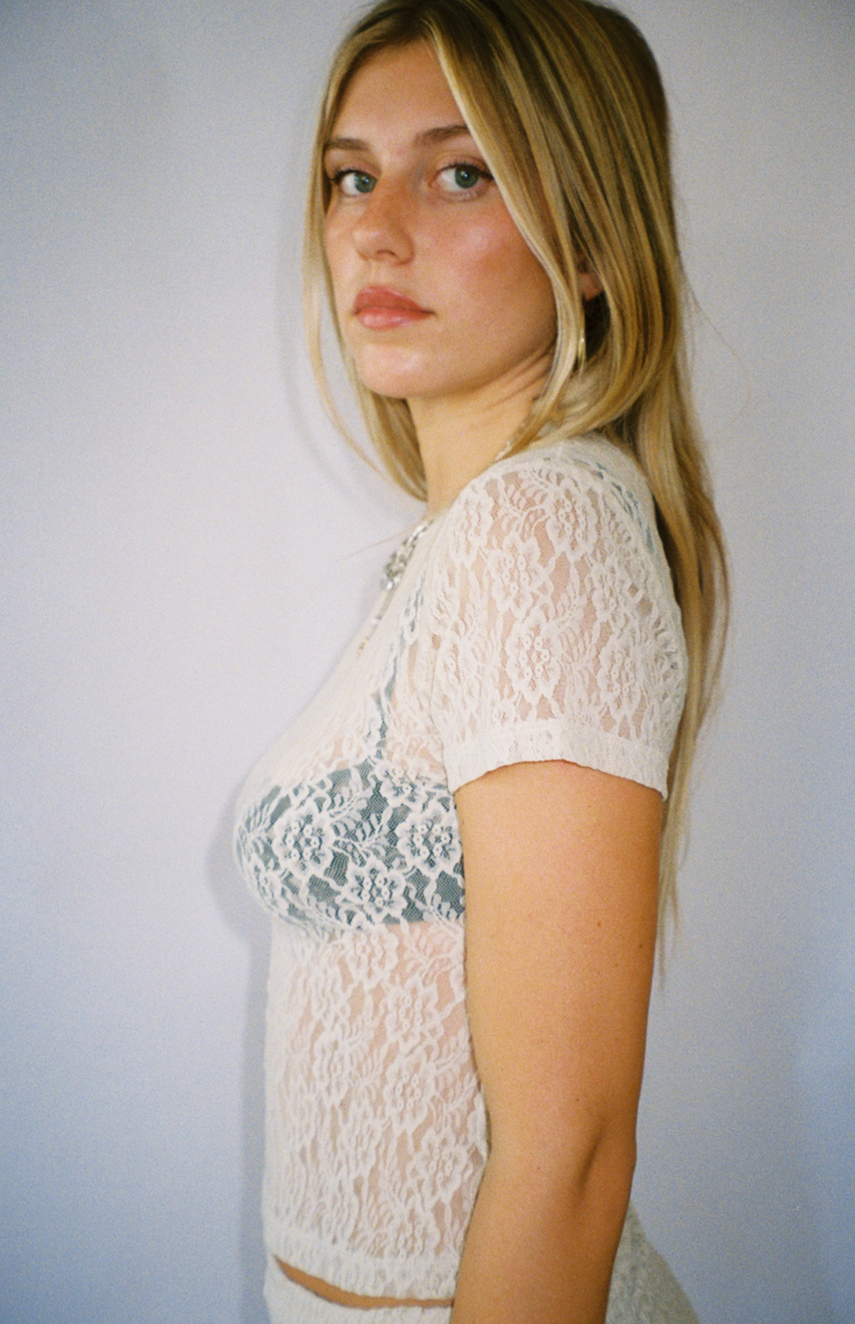 White lace short sleeve crop top with floral pattern and sheer design, worn in side profile view