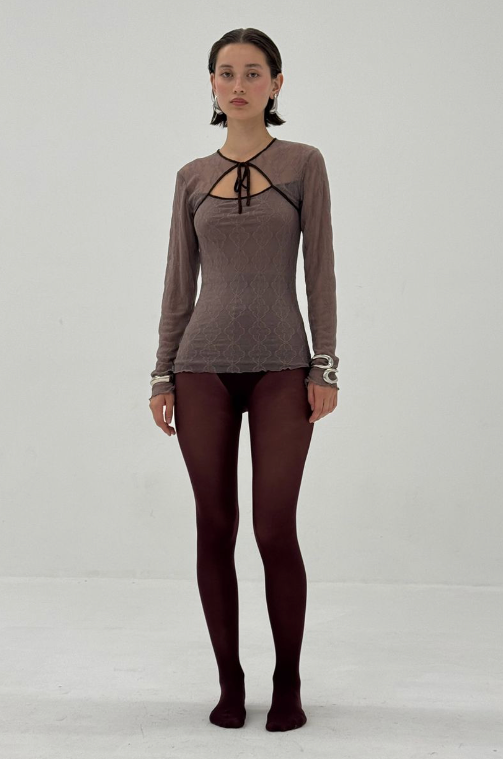 Brown long-sleeve mesh top with cutout neckline and tie detail, paired with burgundy tights
