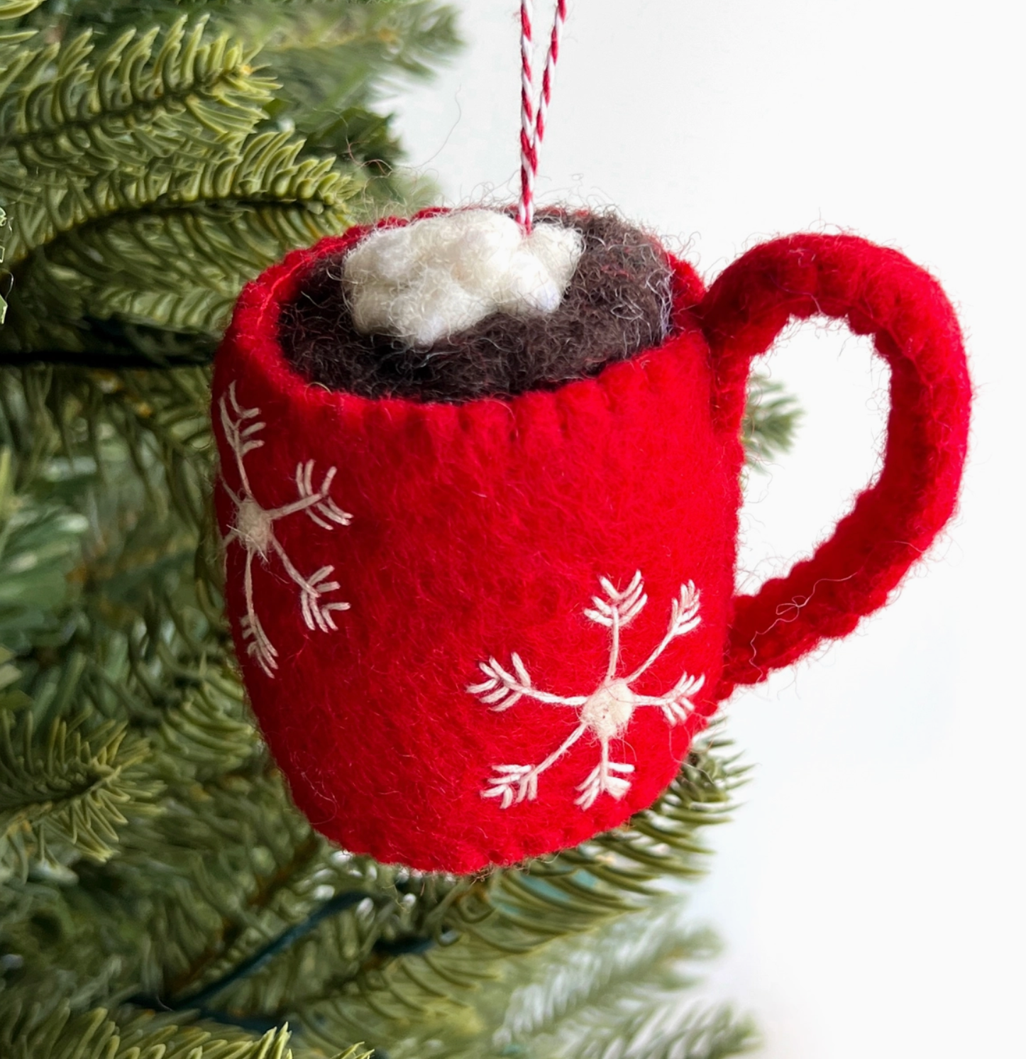 Red felt hot cocoa mug ornament with white snowflake embroidery, brown felt cocoa, and white whipped cream topping