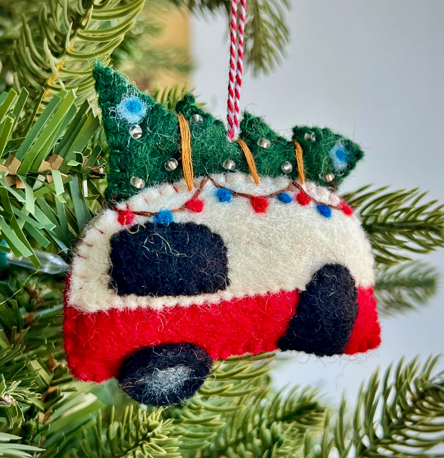 Handmade felt Christmas ornament of red vintage camper with green tree on top, decorated with colorful stitching and beads