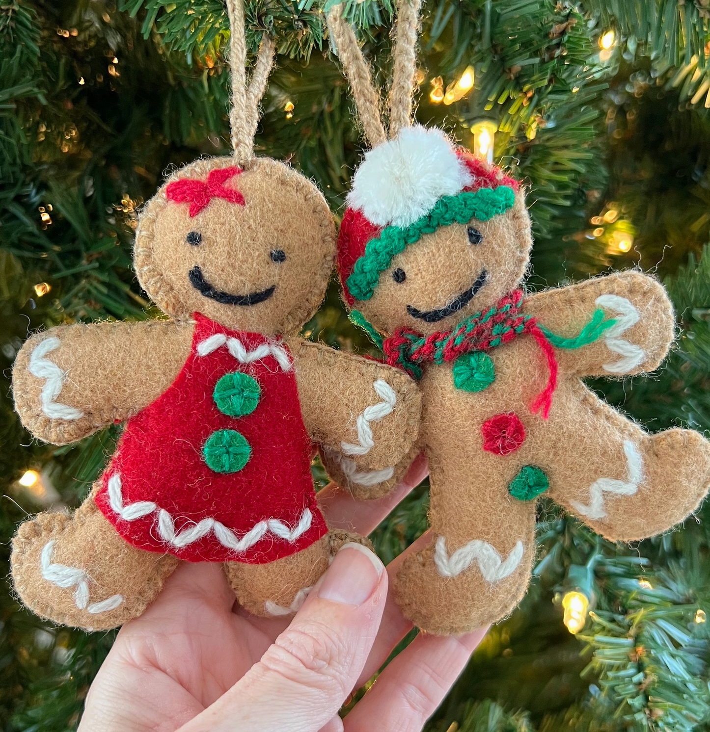 Handmade felt gingerbread ornaments with embroidered details, red and green outfits, white trim, hanging from Christmas tree