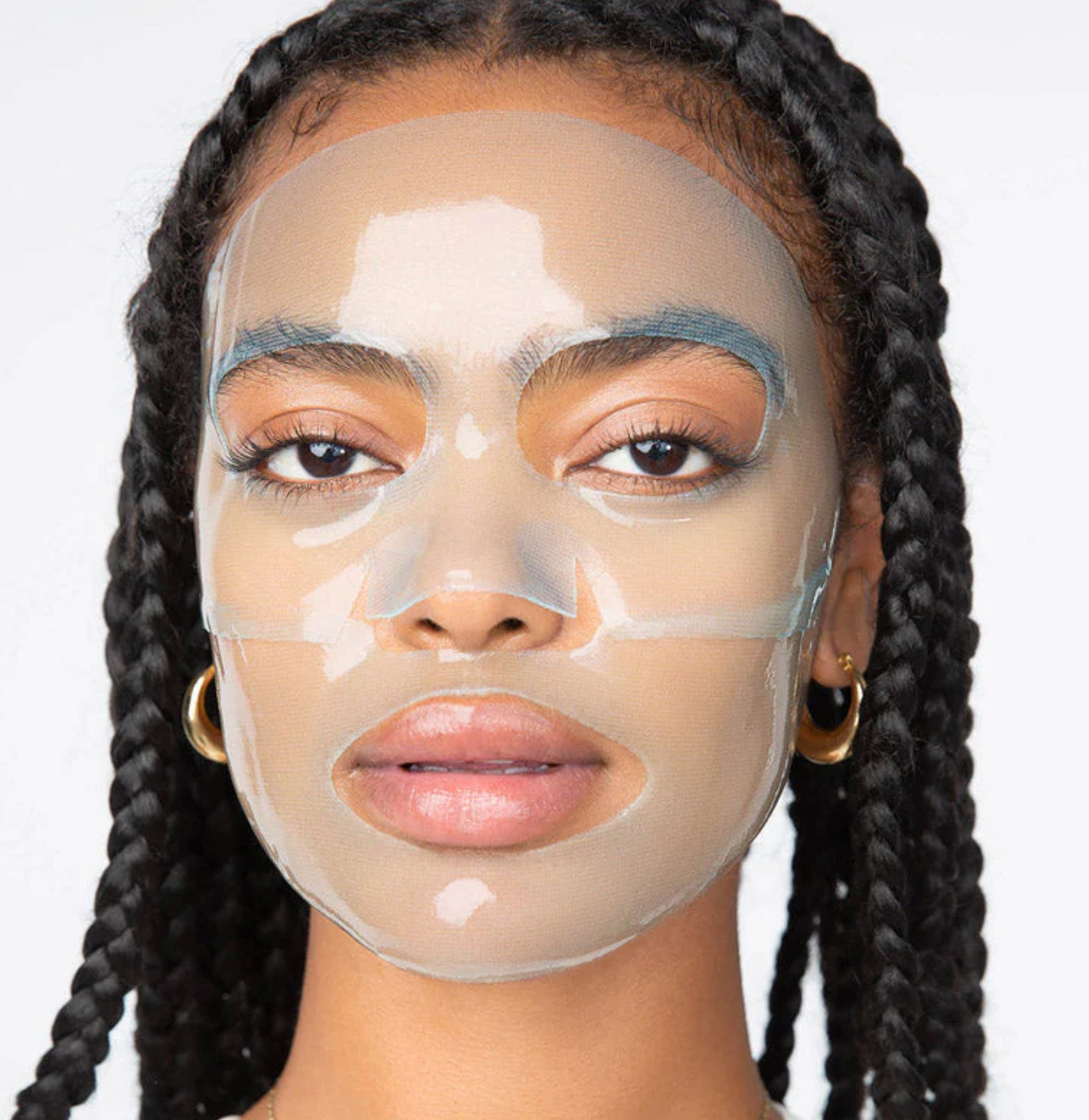 Clear hydrogel face mask with white serum patches on model with braided hair wearing gold hoop earrings