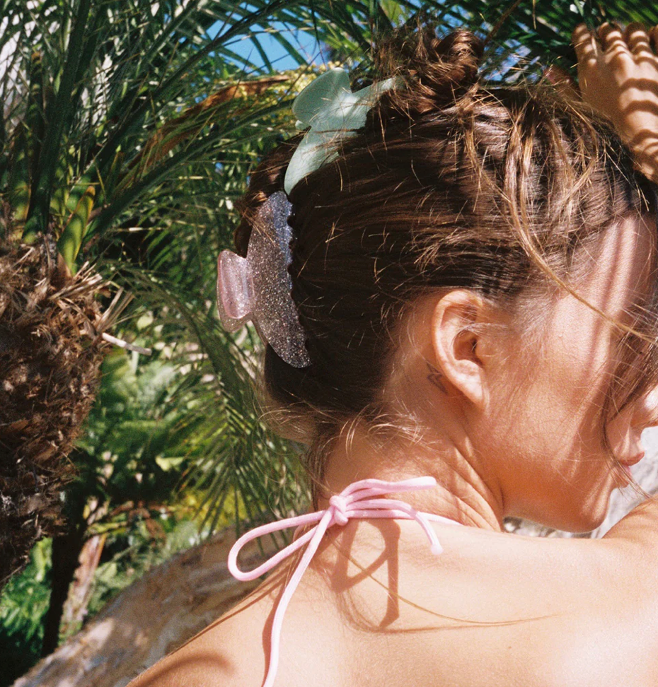 Sparkly purple glitter hair claw clip worn in brown hair with palm trees in tropical background