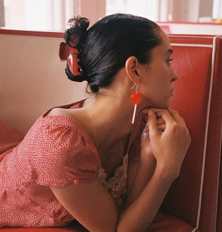 Woman wearing large red circular statement earrings with silver bar detail while seated in retro diner booth