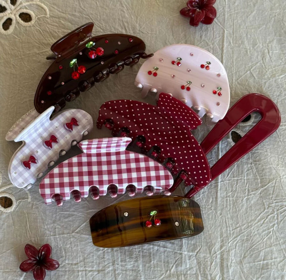 Collection of decorative hair clips and claws in burgundy, pink, and brown with cherry, bow, gingham, and polka dot patterns