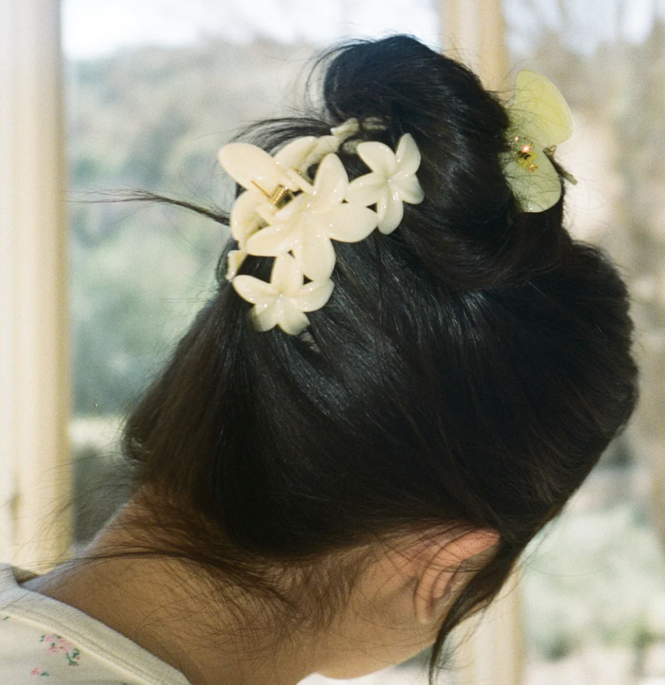 White flower hair clip with butterfly accent on dark updo hairstyle, viewed from behind