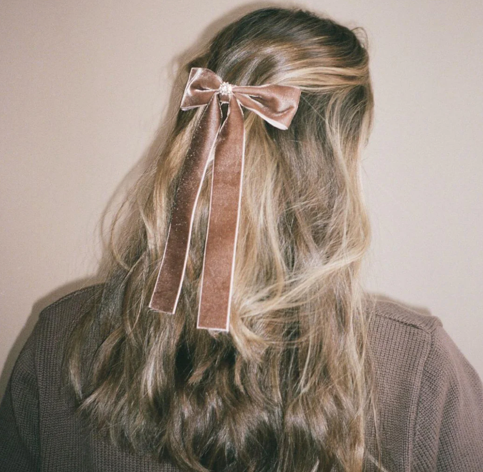 Pink velvet hair bow with long ribbon tails clipped in blonde wavy hair, worn at back of head