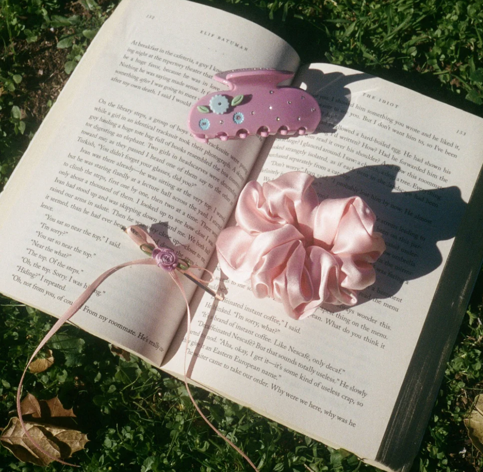 Pink fabric flower headband with decorative teacup fascinator adorned with pearls and rhinestones on open book