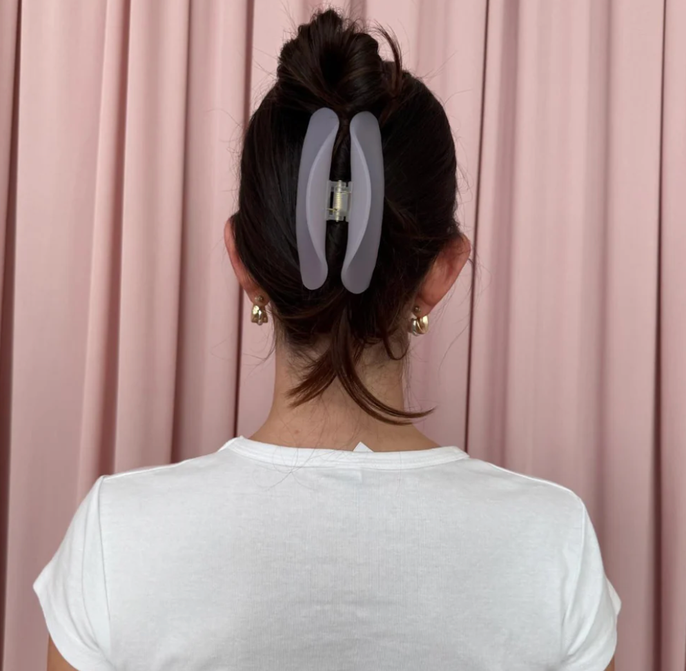 Large translucent gray resin hair claw clip holding dark hair in an updo bun against pink curtain backdrop