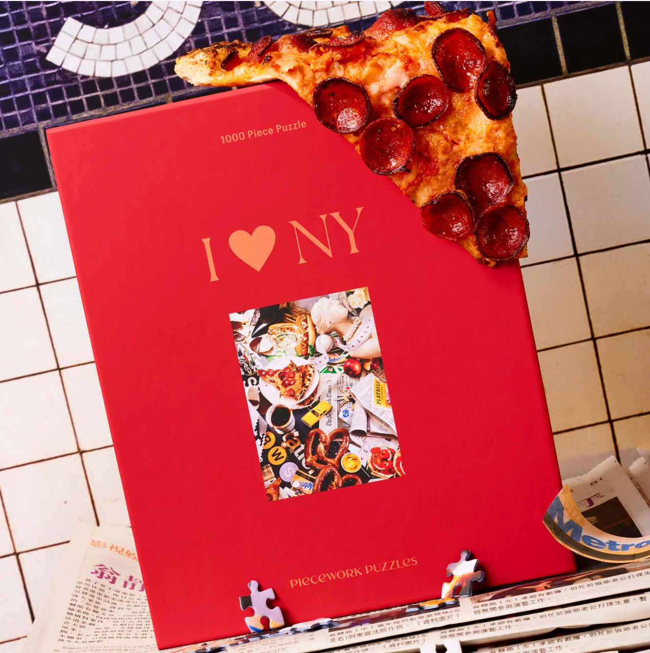Red I Love NY 1000 piece jigsaw puzzle box with pepperoni pizza slice on top, displayed on tiled surface