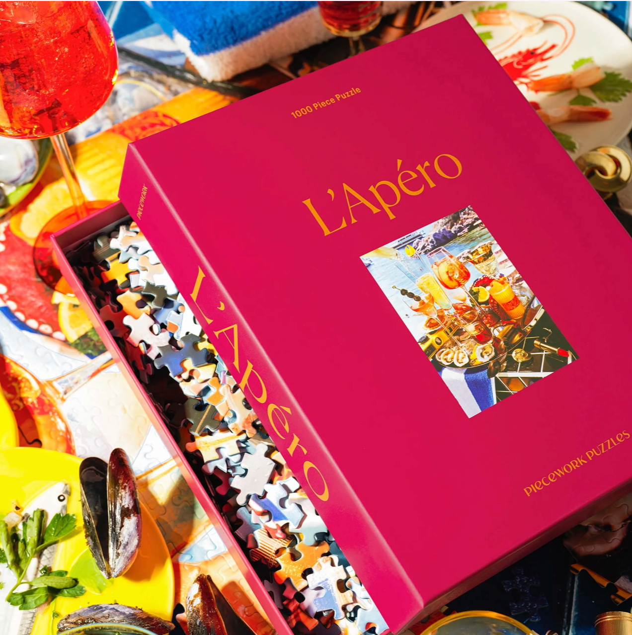 Pink boxed 1000-piece jigsaw puzzle titled L'Apéro showing colorful aperitif scene with drinks and snacks on the cover