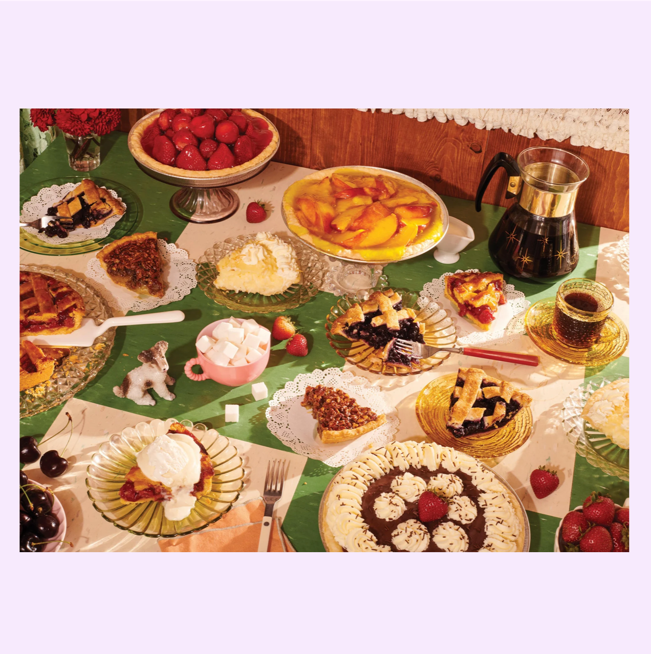 Abundant dessert spread on green tablecloth featuring pies, tarts, waffles, fresh strawberries, coffee, and vintage serveware