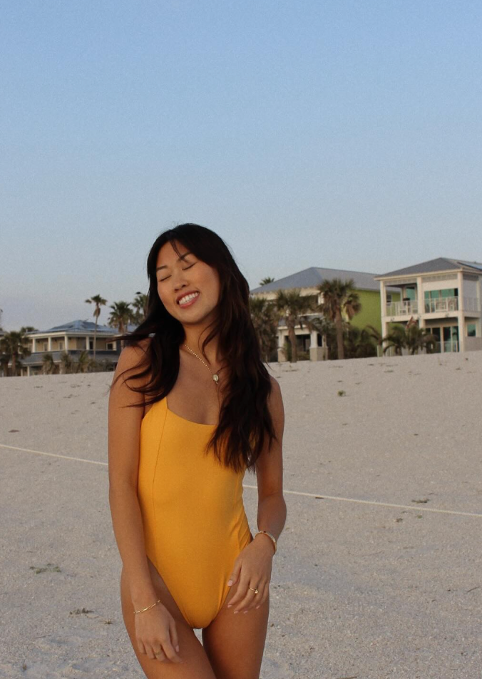 Woman wearing yellow one-piece swimsuit on beach with coastal homes in background