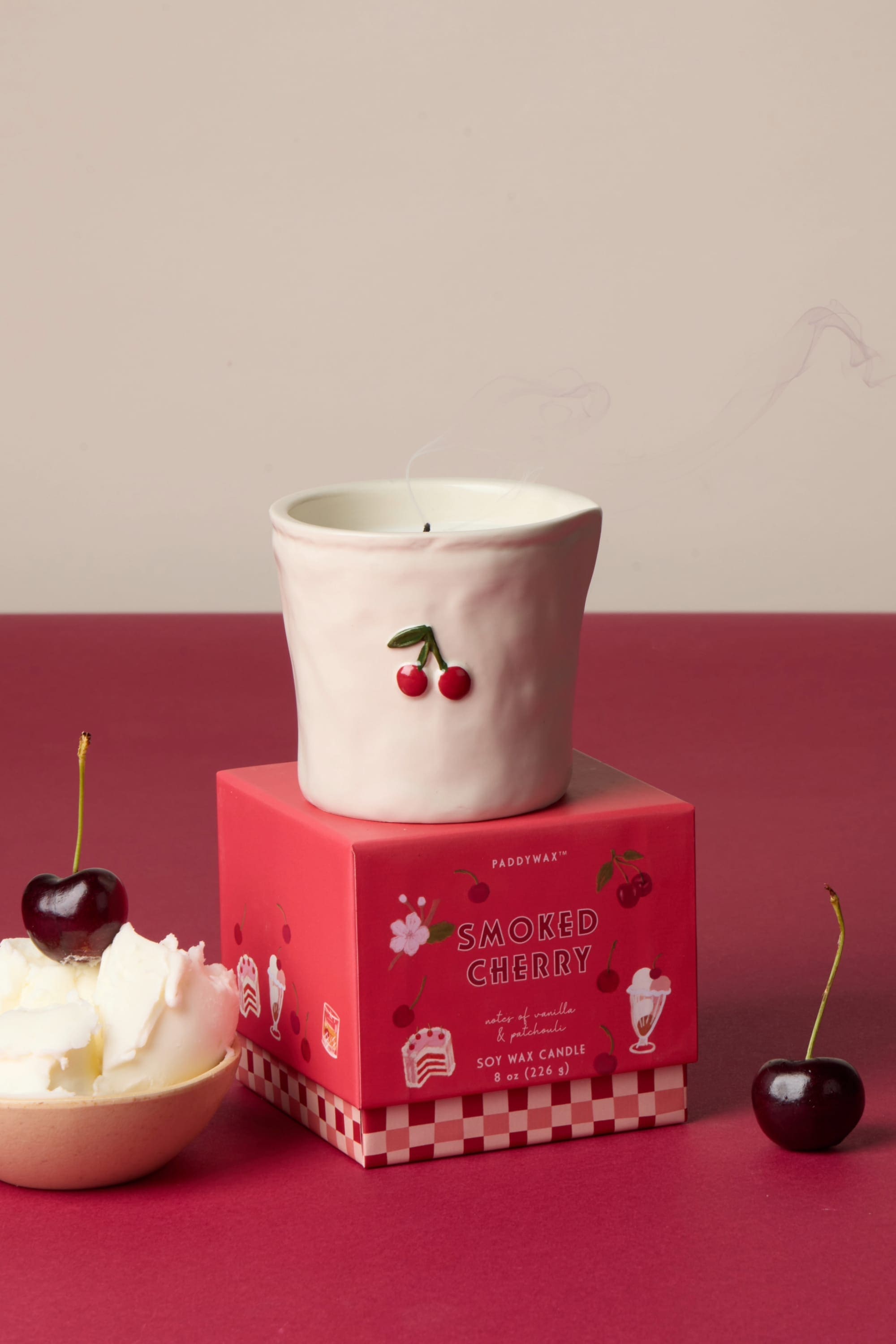 Pink ceramic candle with cherry design on red Smoked Cherry soy wax candle box, styled with fresh cherries and cream