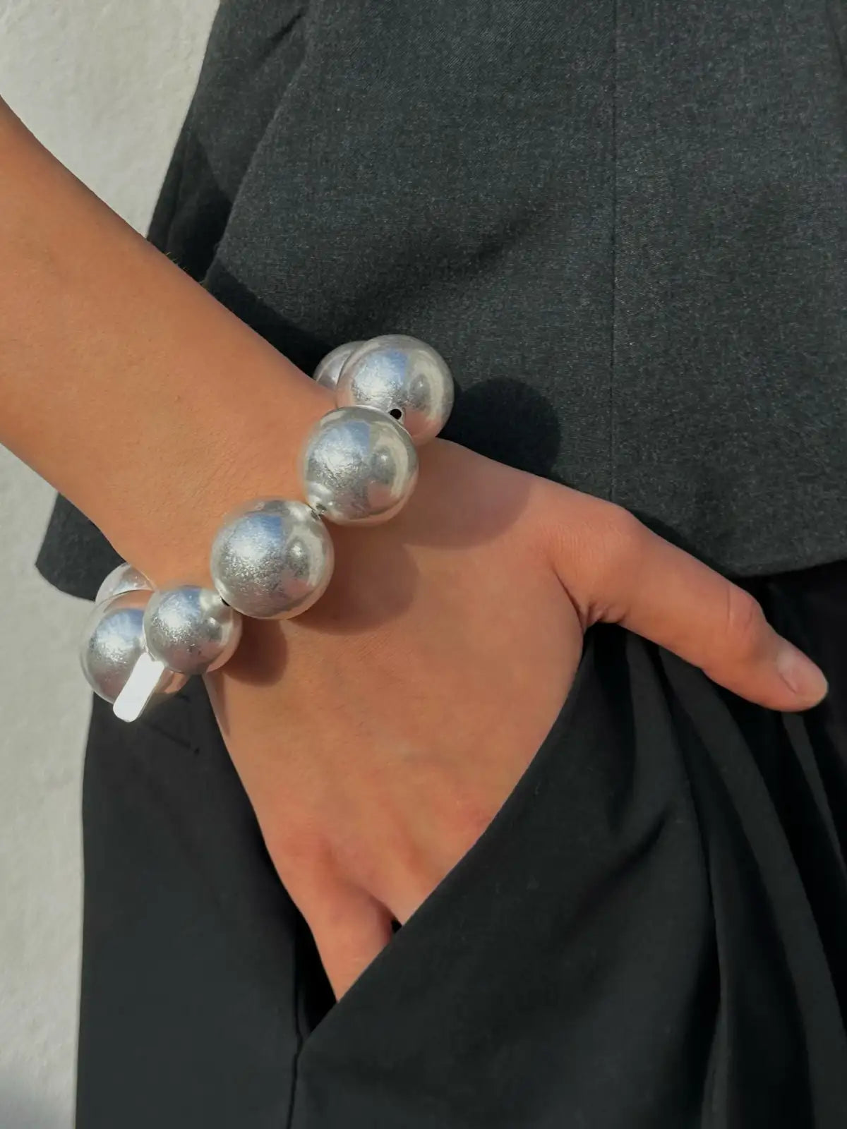 Silver metallic beaded stretch bracelet with large spherical beads on wrist against black dress