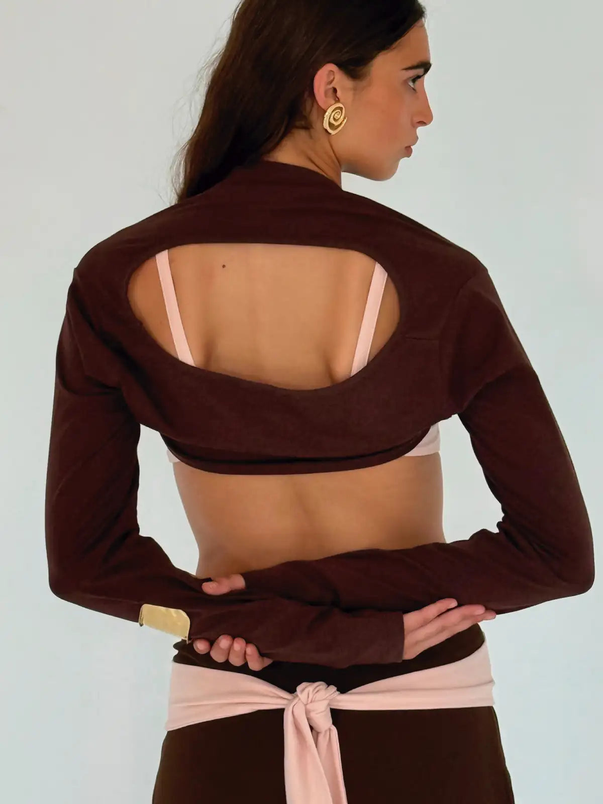 Brown long-sleeve crop top with open back cutout detail and pink sports bra underneath, activewear style