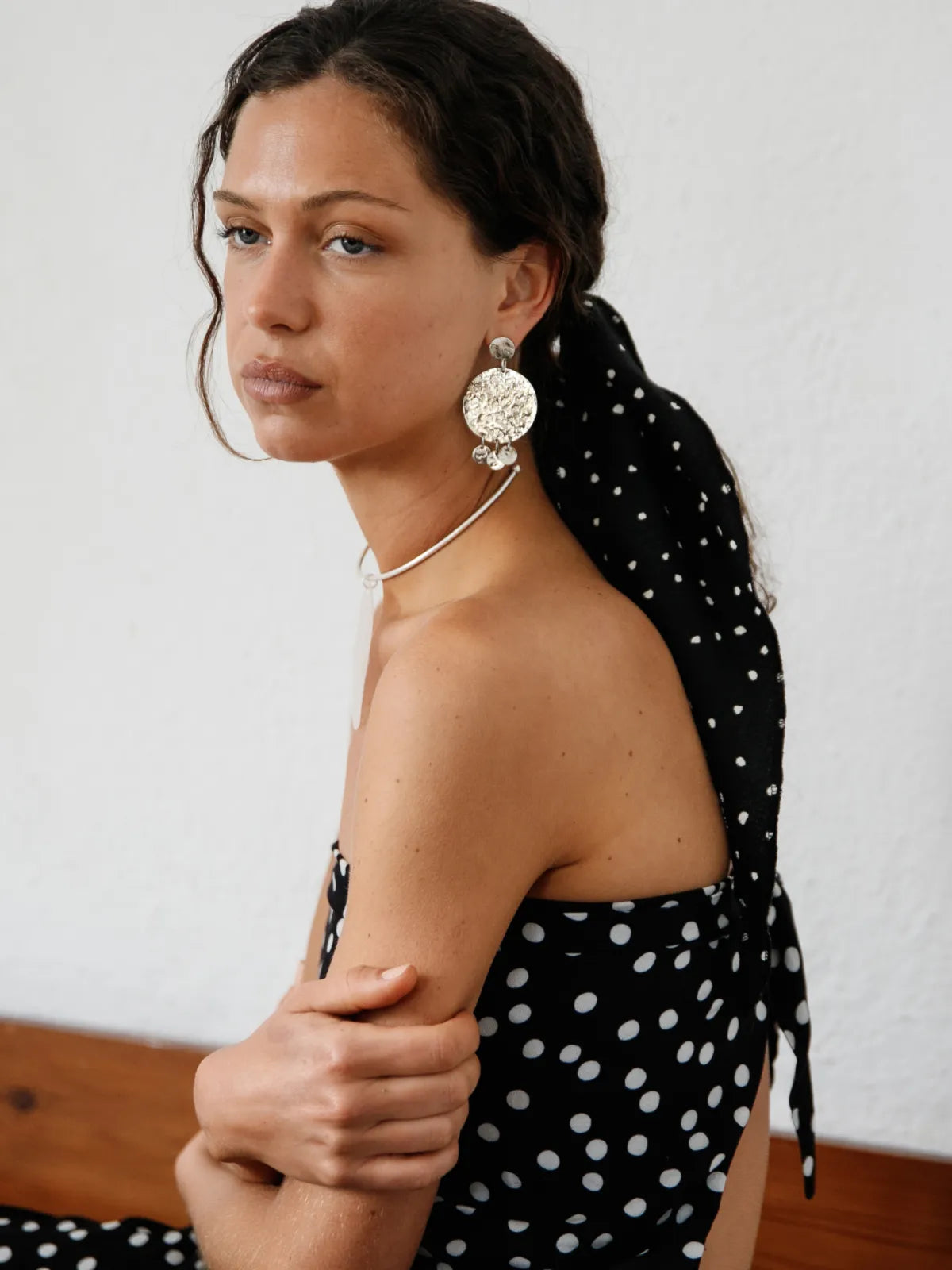 Large hammered silver disc earrings with metallic collar necklace on model wearing black polka dot dress