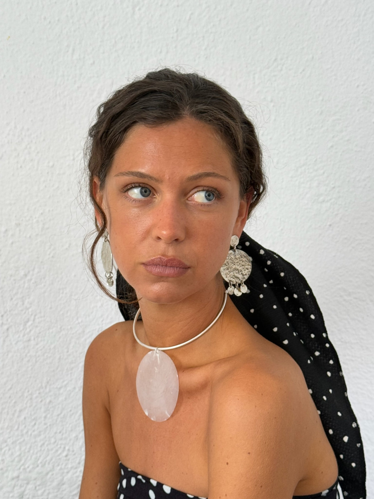 Woman wearing silver hammered disc drop earrings and rose quartz pendant necklace against white background