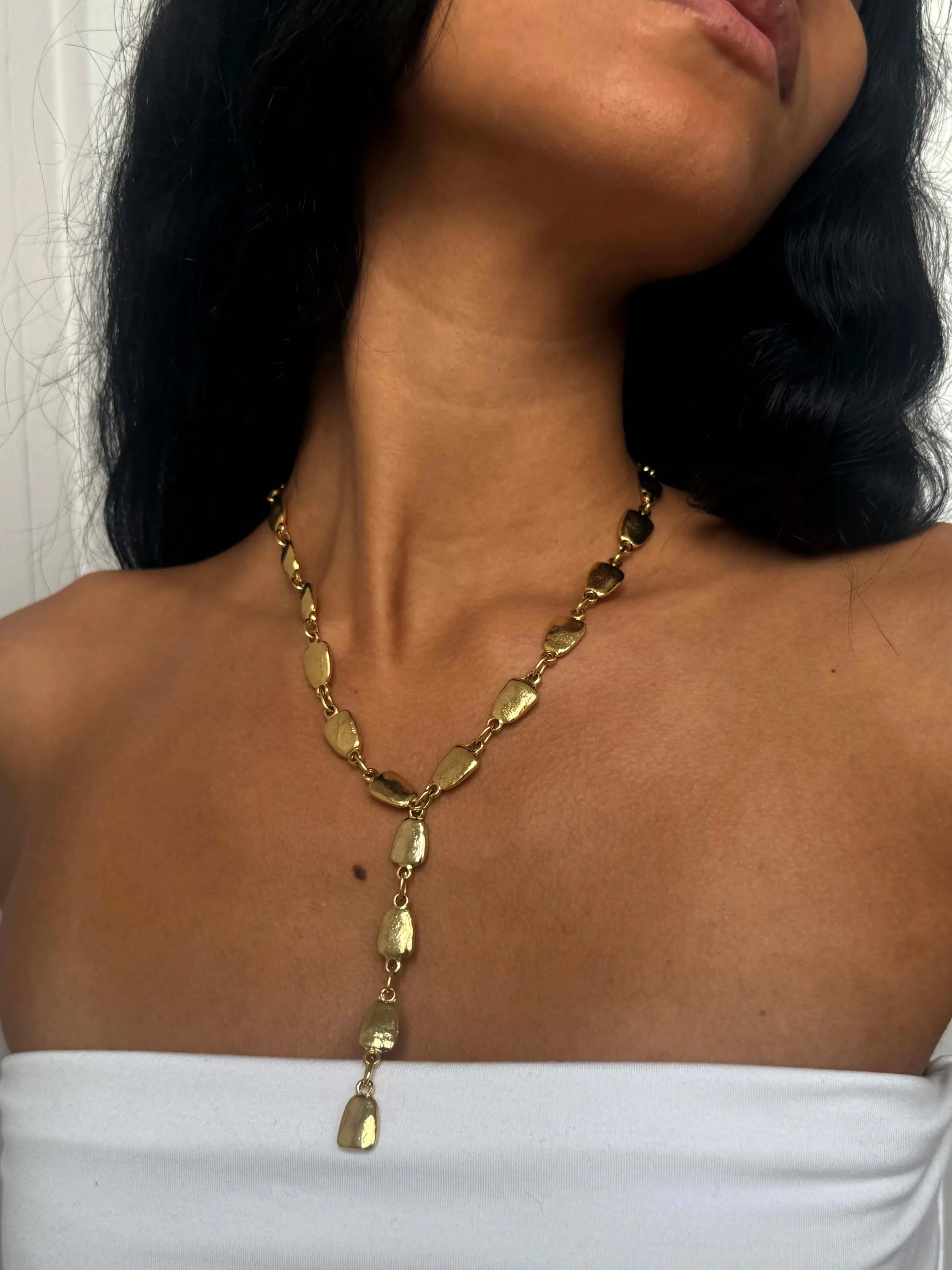 Gold Y-shaped necklace with hammered oval links and drop pendant on model wearing white top