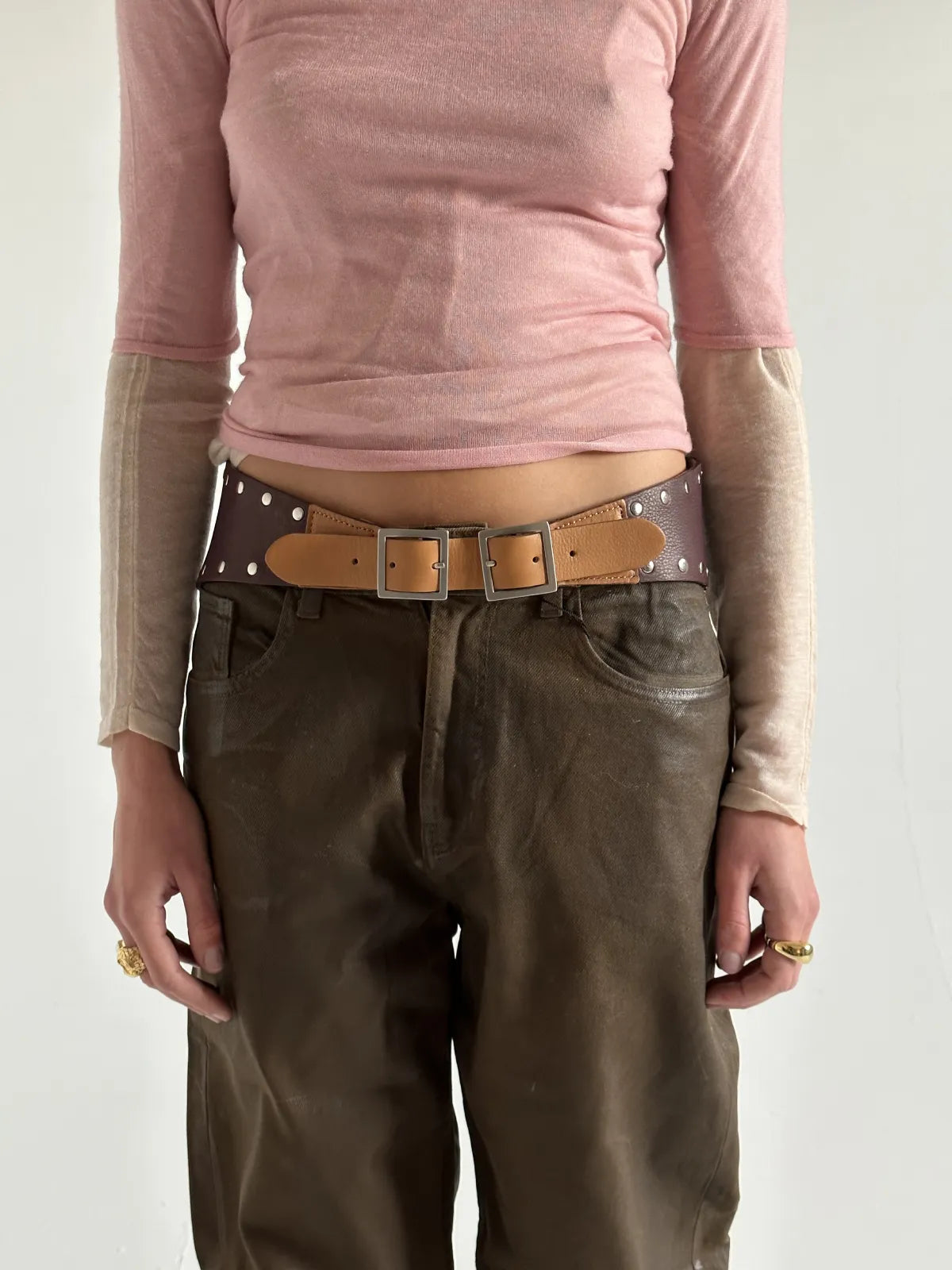 Brown leather double buckle belt with silver studs worn with pink top and olive pants