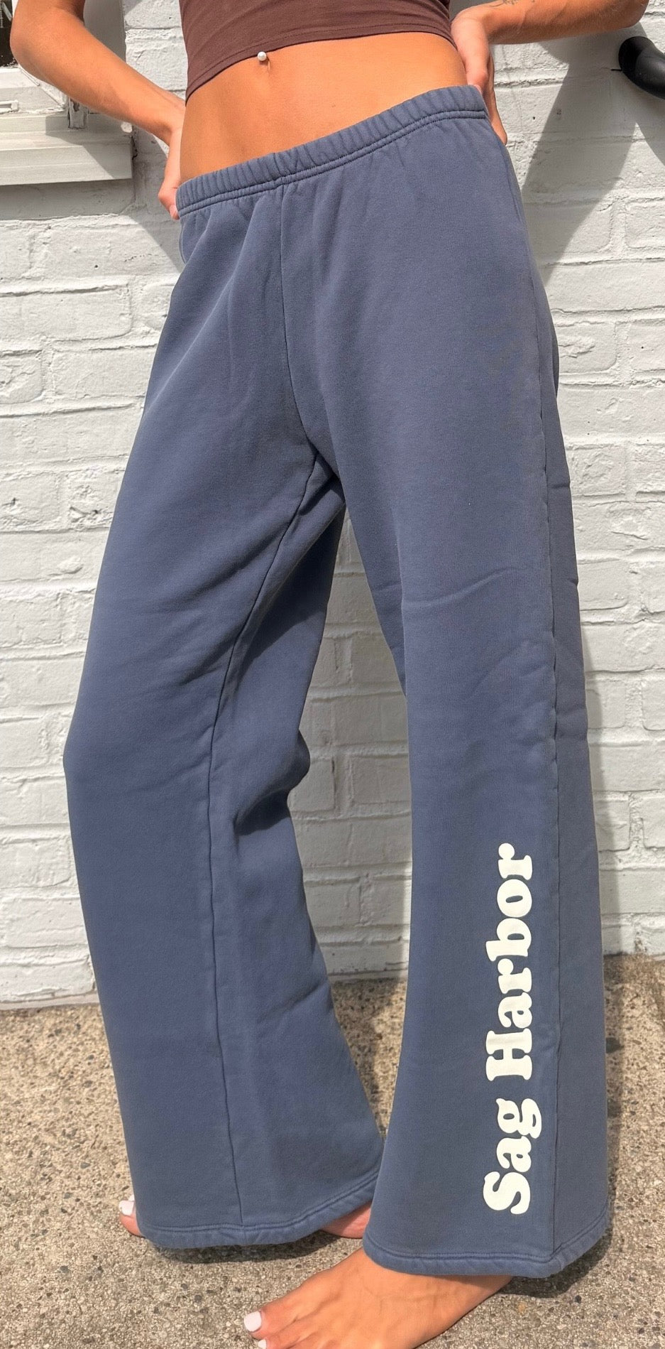 Person wearing blue sweatpants with 'Sag Harbor' text against a light brick wall.