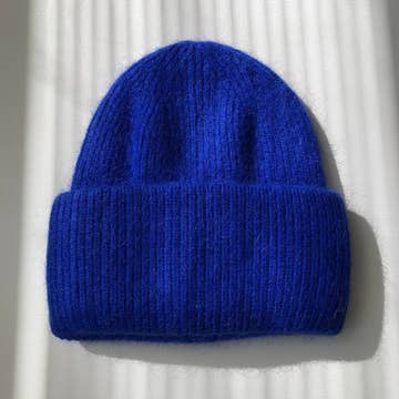 Bright royal blue ribbed knit beanie hat with folded cuff, soft fuzzy wool blend texture, laid flat on white surface.