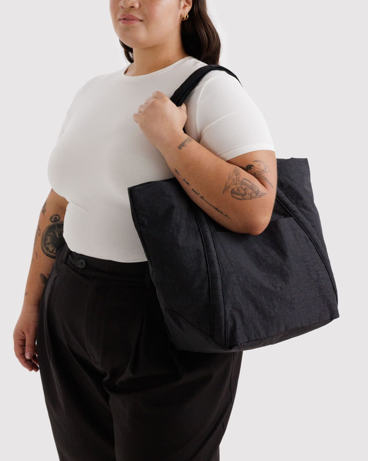 Black canvas tote bag with shoulder strap and exterior pocket, carried by person wearing white shirt and black pants