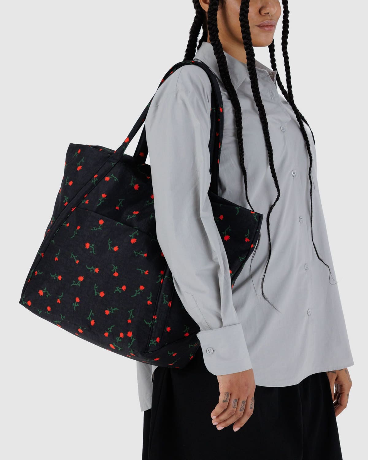 Black tote bag with red rose print pattern carried on shoulder, featuring matching handles and rectangular shape