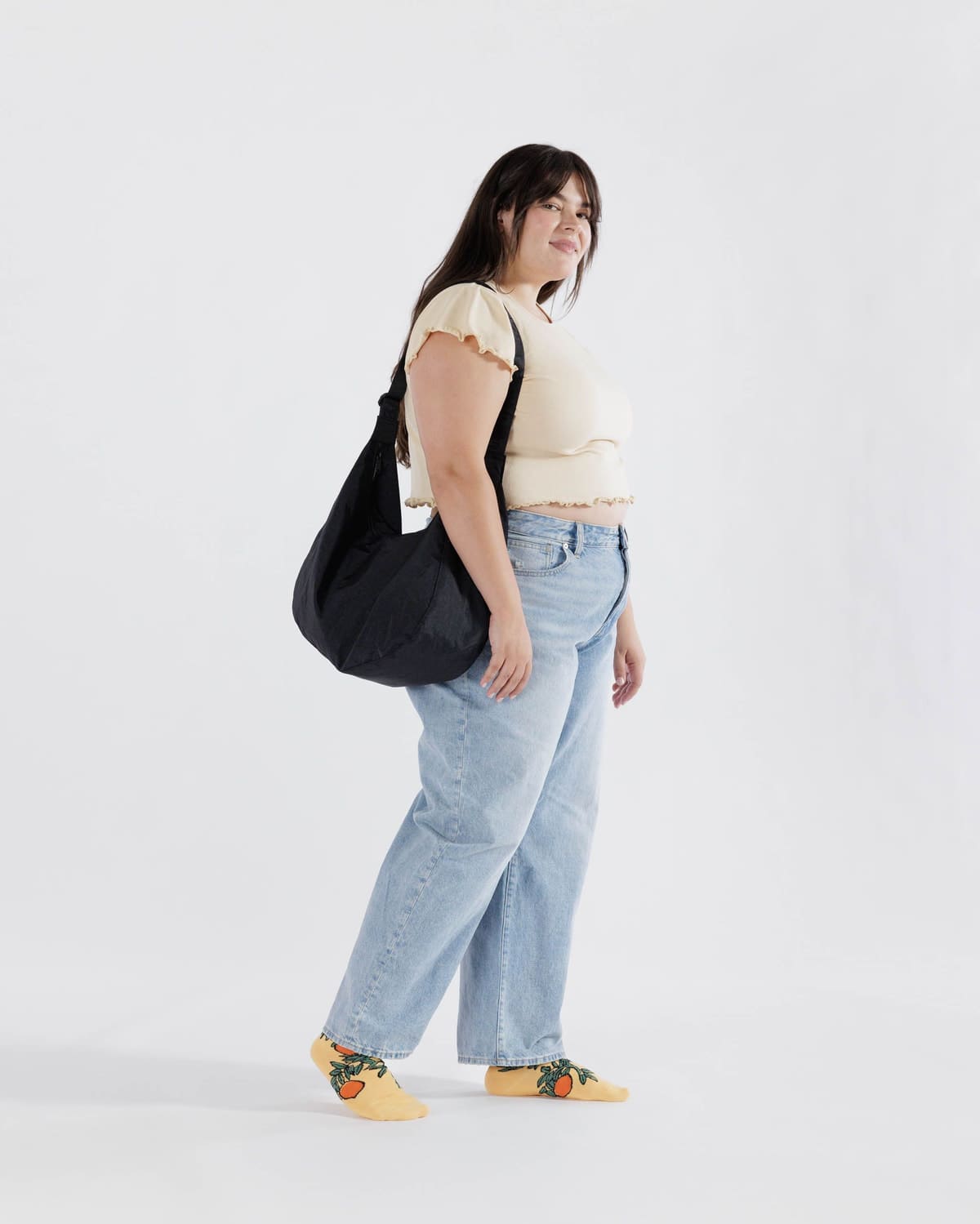 Black canvas shoulder bag with curved slouchy shape worn by person in casual outfit against white background