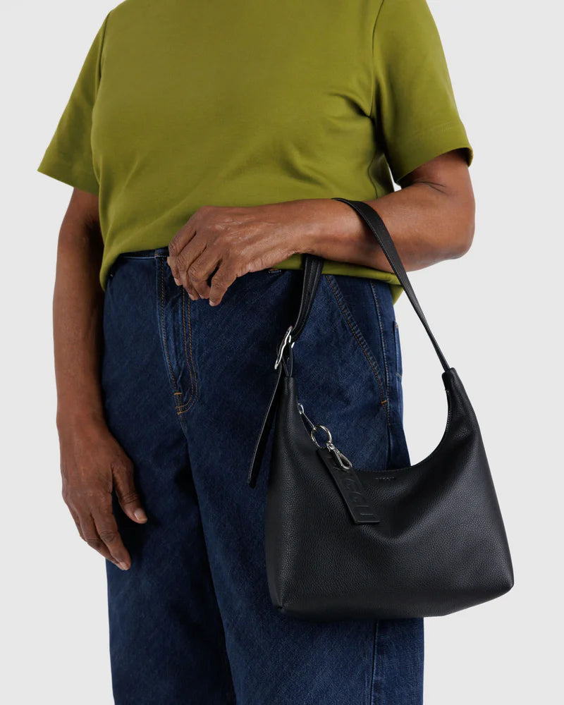Black leather mini hobo bag with shoulder strap worn by person in olive t-shirt and blue jeans