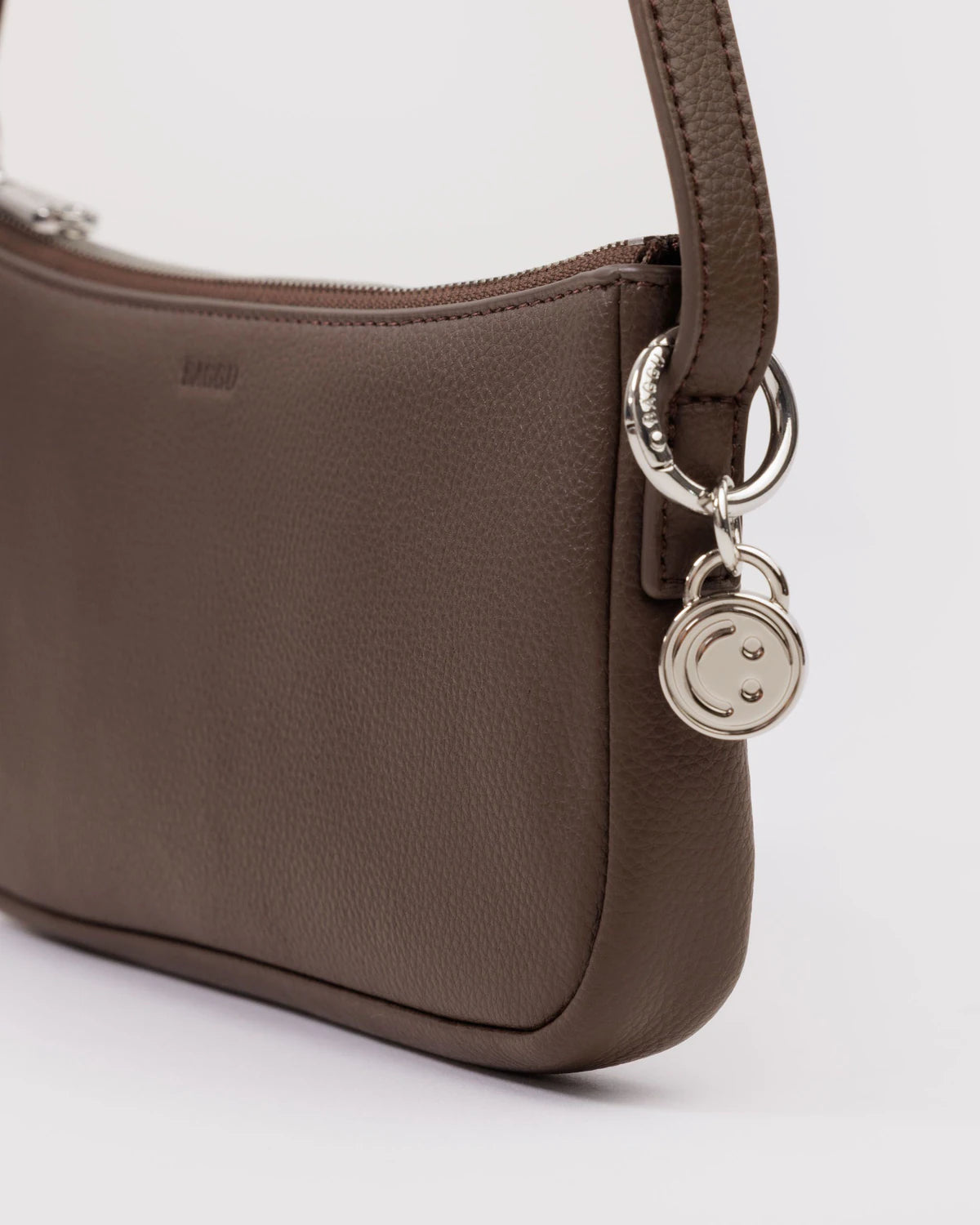 Brown leather shoulder bag with silver smiley face charm and zipper closure detail