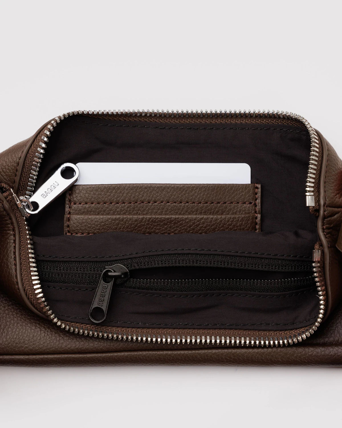 Brown leather toiletry bag opened to show black interior with zippered pocket and compartment holding white Baxter branded item