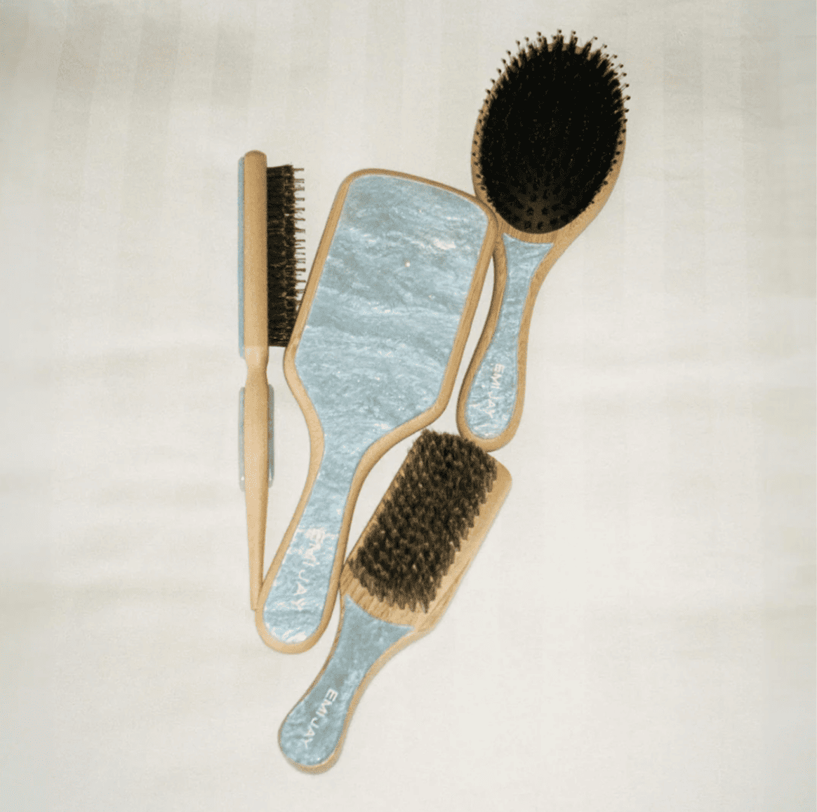 Set of four hair brushes with natural bristles and wooden handles in light blue and natural wood tones