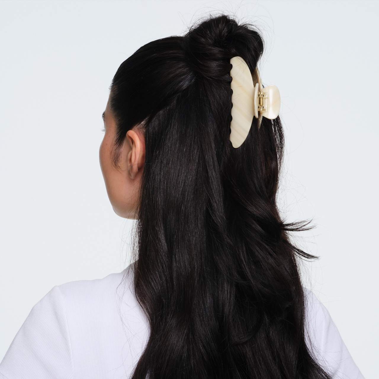 Cream-colored wavy resin hair claw clip with gold clasp securing half-up hairstyle in dark hair