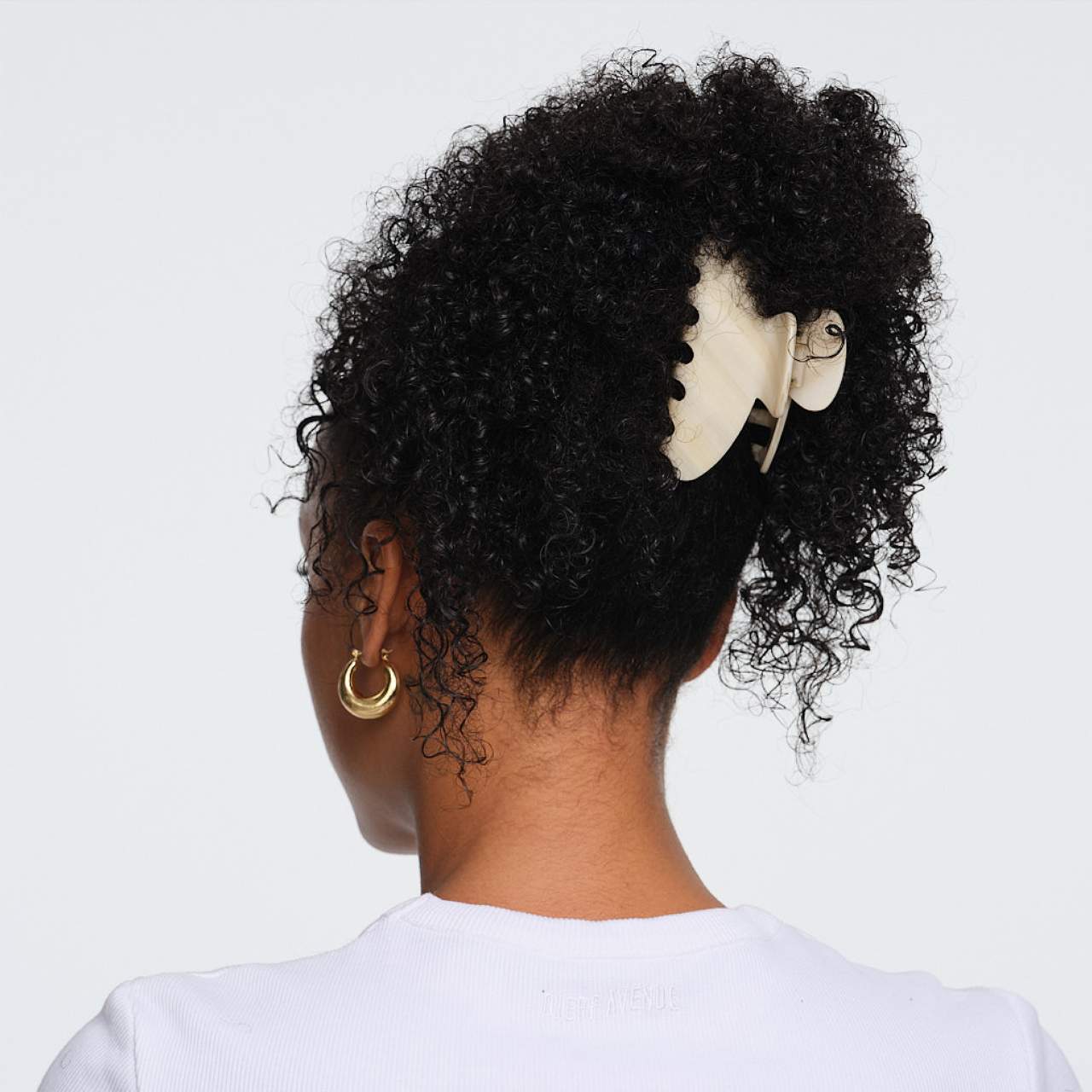 Black curly hair styled in high ponytail with gold hoop earring visible, shown from behind on white background