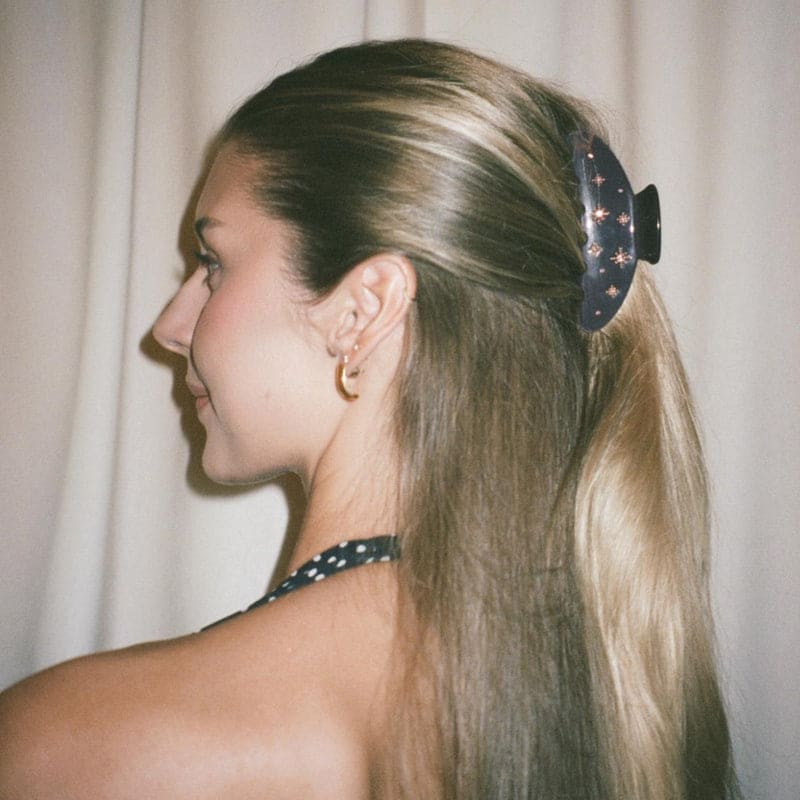 Navy blue hair claw clip with star pattern securing blonde hair in half-up style