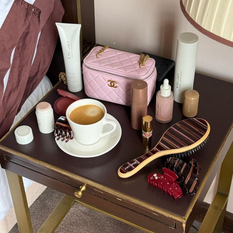 Pink quilted makeup bag with gold chain strap and CC logo sitting on vanity table with beauty products and coffee