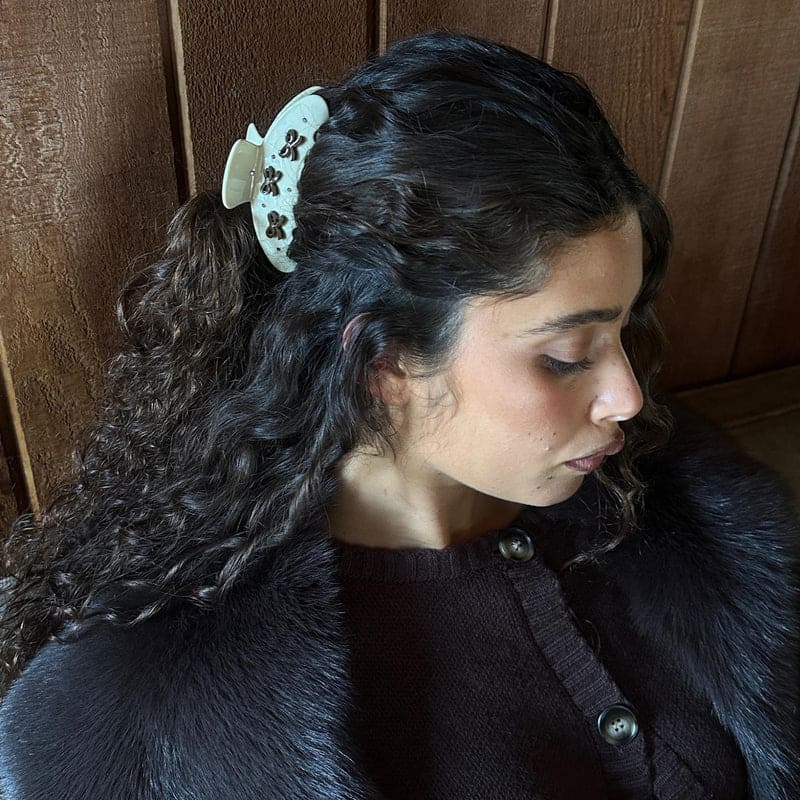 White crochet scrunchie with brown paw print pattern worn in dark curly hair against wooden background