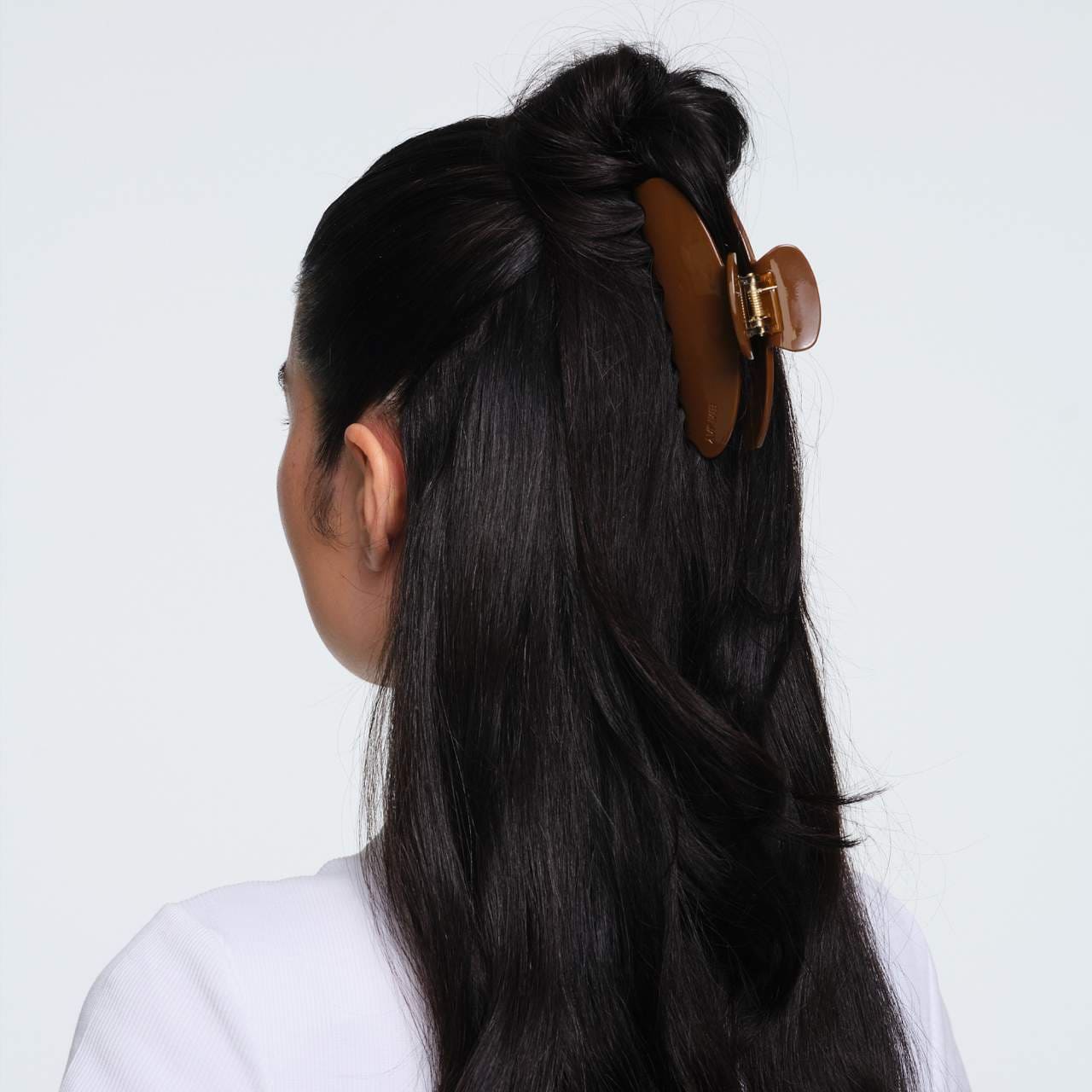 Brown tortoiseshell hair claw clip with gold clasp securing half-up hairstyle in dark black hair