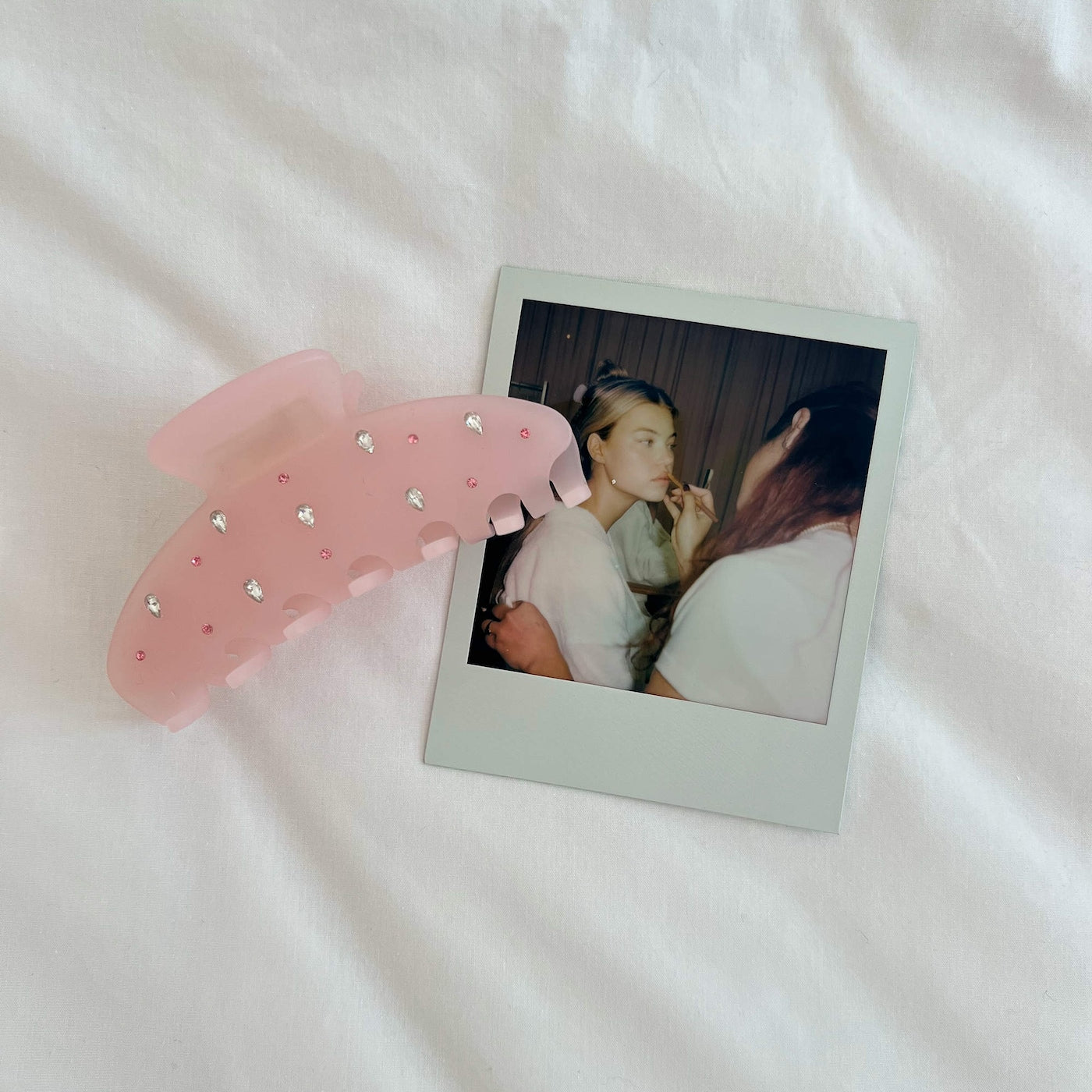 Pink embellished organza hair scrunchie with rhinestone and flower details next to instant photo on white fabric