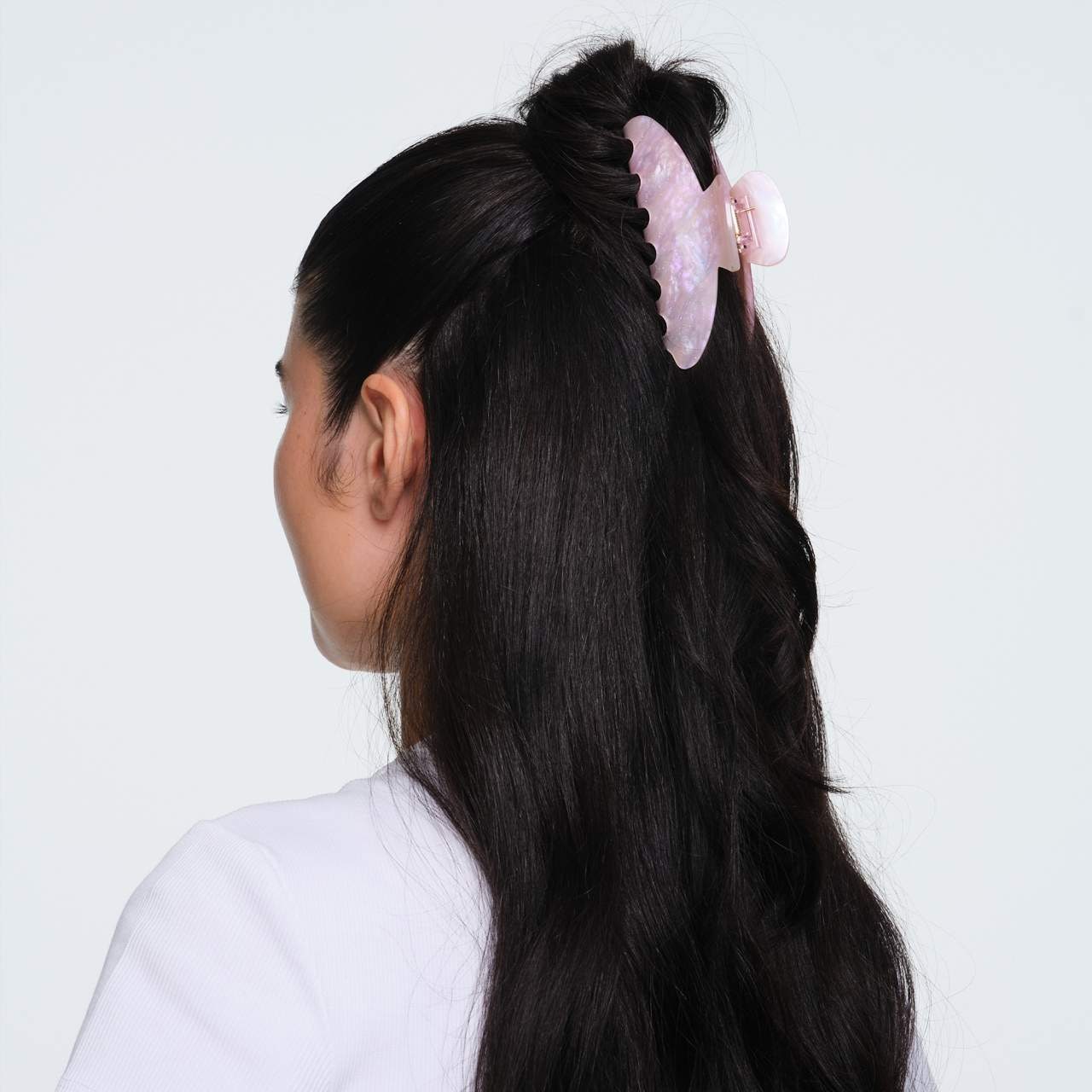 Pink marbled resin hair claw clip securing a half-up hairstyle on long black hair against white background