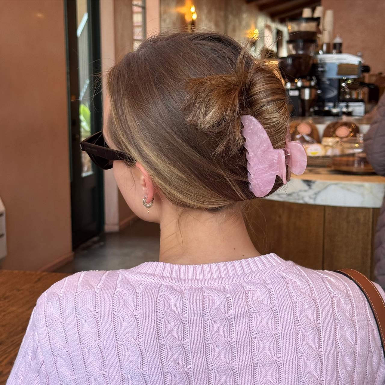 Pink butterfly hair claw clip holding an updo hairstyle on brown hair, worn with matching pink cable-knit sweater