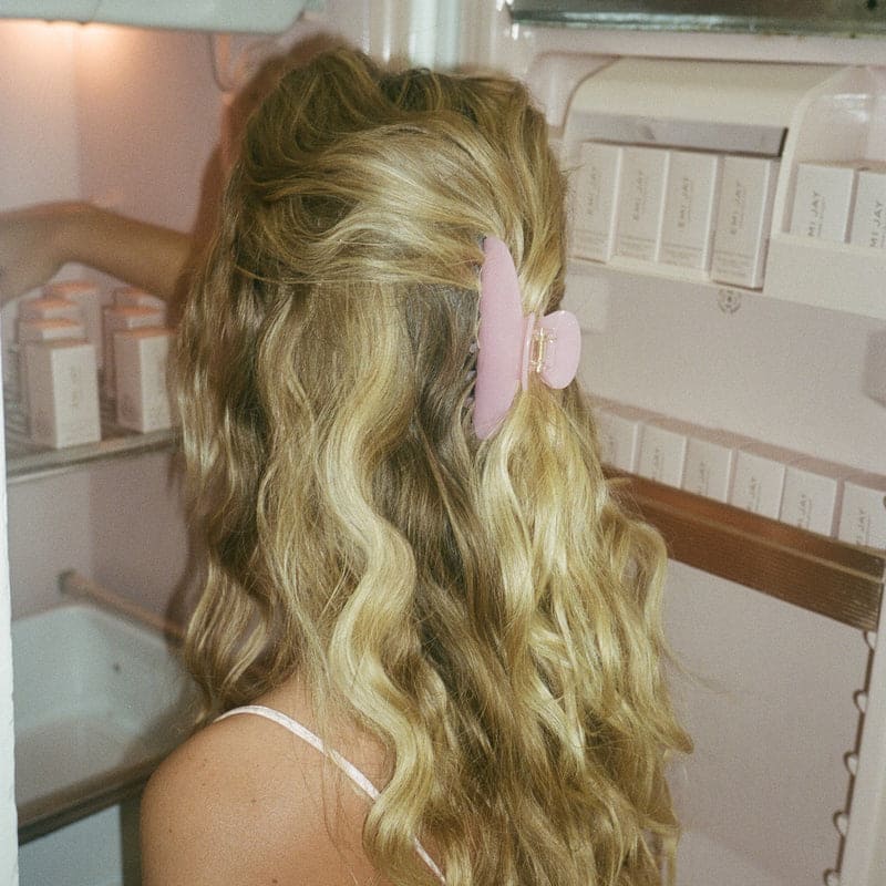 Pink butterfly hair clip securing half-up wavy blonde hair in bathroom setting