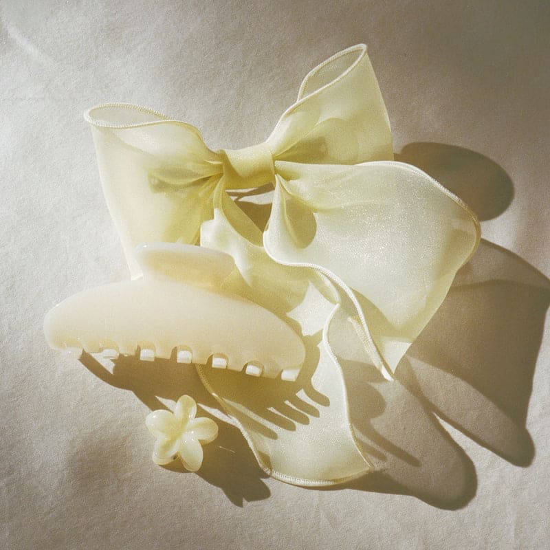 Cream colored satin hair bow clip with decorative comb attachment and small flower accent