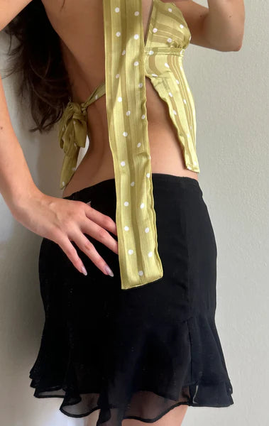 Yellow polka dot wrap top with tie detail and black ruffle mini skirt outfit on model